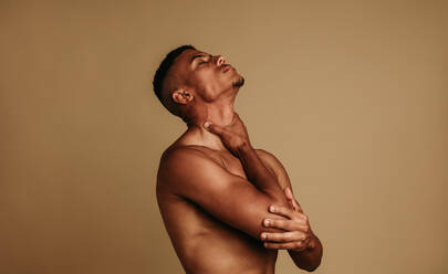 Portrait of african american man standing on brown background feeling suffocated. Shirtless fit man holding his throat with his hand. - JLPSF06624