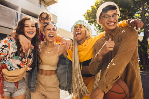 Group of generation z friends laughing together outdoors. Cheerful young friends embracing each other in the summer sun. Youngsters having fun and enjoying their youth. - JLPSF06759