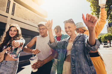 Tanzschritte in der Stadt. Eine Gruppe von Freunden der Generation Z tanzt fröhlich, während sie zusammen in der Sommersonne spazieren gehen. Glückliche junge Freunde, die Spaß haben, während sie zusammen im Freien abhängen. - JLPSF06764