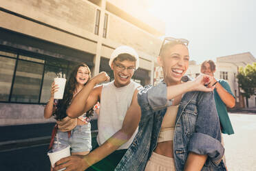 Smiling group of friends having fun outdoors. Group of generation z friends dancing cheerfully while walking together in the summer sun. Happy young friends hanging out together in the city. - JLPSF06765