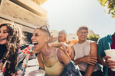 Eine Gruppe von Freunden der Generation Z, die fröhlich lachen, während sie in der Sommersonne spazieren gehen. Glückliche junge Freunde, die Spaß haben, während sie zusammen im Freien abhängen. - JLPSF06768