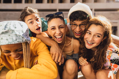 Quality time with friends. Group of generation z friends laughing cheerfully while hanging out together outdoors in the city. Happy young friends having fun together in the summer sun. - JLPSF06777