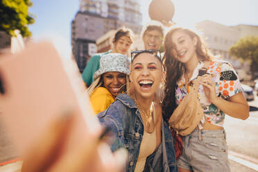 Freunde machen ein Selfie in der Sonne. Eine Gruppe von Freunden der Generation Z hat Spaß, während sie zusammen in der Stadt abhängen. Multiethnische junge Menschen, die ihre glücklichen Momente festhalten. - JLPSF06791