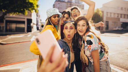 Verrückte Momente einfangen. Eine Gruppe glücklicher Freunde der Generation Z, die Selfies machen, während sie zusammen in der Stadt abhängen. Multiethnische junge Menschen, die gemeinsam Spaß in der Sommersonne haben. - JLPSF06793