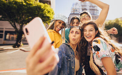 Lebhafte junge Leute machen ein Selfie zusammen. Fröhliche Freunde der Generation Z, die Spaß haben, während sie zusammen in der Stadt abhängen. Eine multiethnische Gruppe von Freunden, die ihre glücklichen Momente in der Sonne festhalten. - JLPSF06795