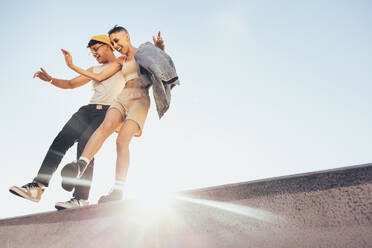 Zwei fröhliche Freunde tanzen und haben Spaß im Freien. Zwei glückliche Freunde stehen auf einer Mauer mit dem Himmel im Hintergrund. Junger Mann und Frau fühlen sich energiegeladen und voller Leben. - JLPSF06831