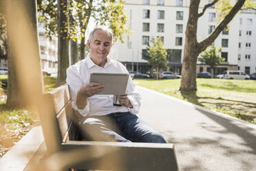 Älterer Mann mit Tablet-PC auf einer Bank sitzend - UUF27518