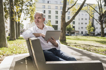 Nachdenklicher älterer Mann mit Tablet-PC auf einer Bank sitzend - UUF27521