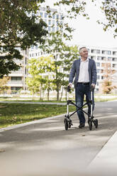 Glücklicher älterer Mann, der mit einer Gehhilfe auf dem Gehweg spazieren geht - UUF27546