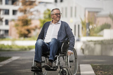 Lächelnder älterer Mann im Rollstuhl in der Stadt - UUF27556