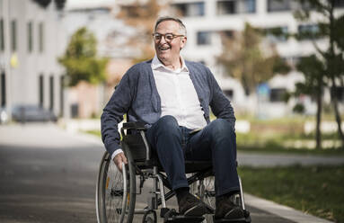 Happy senior man sitting on wheelchair in the city - UUF27557