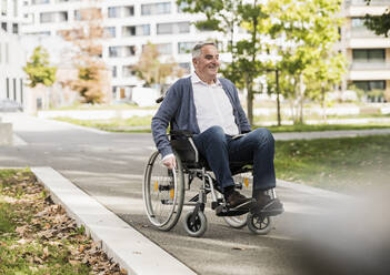 Smiling senior man in sweater sitting on wheelchair - UUF27558