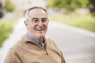 Happy senior man wearing eyeglasses on footpath - UUF27569