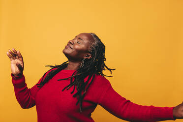 Happy black woman with dreadlocks dancing and having fun while standing against a studio background. Joyful mature woman embracing her natural hair with pride. - JLPSF06889