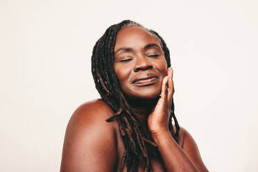 Beautiful woman with dreadlocks touching her flawless skin with her eyes closed. Confident dark-skinned woman embracing her smooth melanated skin. Mature black woman ageing gracefully. - JLPSF06897