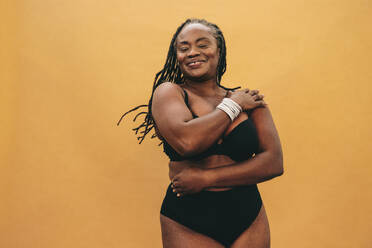 Happy black woman embracing her natural body. Smiling woman standing  against a studio background in black