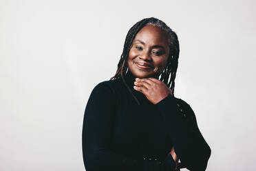 Happy mature woman with dreadlocks looking at the camera with a smile in a studio. Fashionable middle-aged woman standing against a grey background. - JLPSF06950