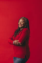 Carefree woman with dreadlocks smiling happily while standing against a red background. Mature black woman embracing her natural hair with pride. - JLPSF06951