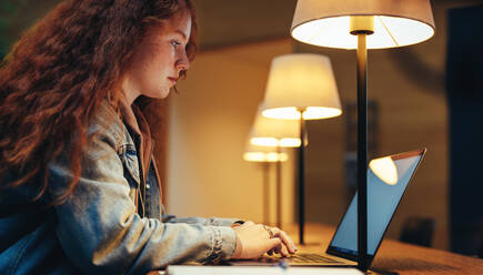 Mädchen in der Bibliothek in der Nacht mit Laptop. Studentin studiert am Laptop spät in der Nacht in der College-Bibliothek - JLPSF06981