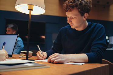 Student macht sich Notizen in der Bibliothek. Junger Mann in der Bibliothek beim Studieren. - JLPSF06990