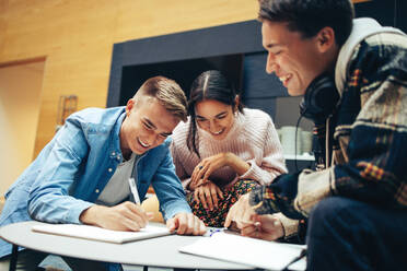 Junger Mann erklärt seinen Freunden in der Universität ein Projekt. Zufriedene Studenten diskutieren über ihre Studien. - JLPSF06995