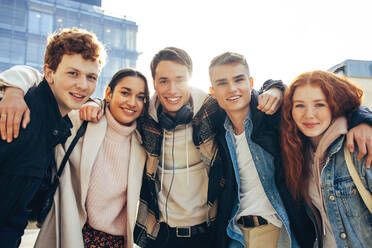 Lächelnde junge Freunde, die zusammen auf dem Campus stehen. College-Studenten mit Händen auf den Schultern und lächeln in die Kamera. - JLPSF06997