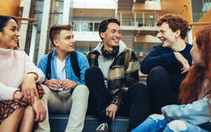 Glückliche Studenten, die auf einer Treppe sitzen und sich unterhalten, eine Gruppe von Jungen und Mädchen, die ihre Pause genießen. - JLPSF07002