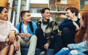 Happy university students sitting and talking on steps. Group of boys and girls enjoying their break time in college. - JLPSF07002