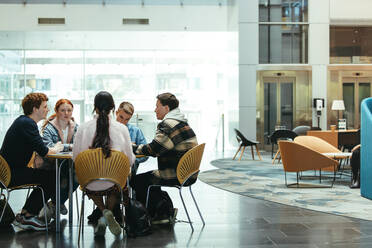 Eine Gruppe von vier jungen Leuten sitzt um einen Tisch und lernt auf dem Campus einer Hochschule. Studenten diskutieren ein Projekt in der Lobby der Hochschule. - JLPSF07020