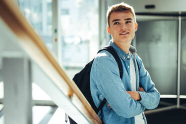 Student, der an einem Geländer steht und wegschaut. Junger Mann mit verschränkten Armen auf einem College-Campus. - JLPSF07021