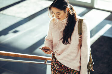 Studentin, die ihr Handy benutzt und die Treppe in der High School hinaufgeht. Junge Frau, die ihren Social-Media-Status überprüft, bevor sie zum Unterricht geht. - JLPSF07025