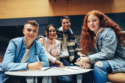 Schüler, die in der High School Gruppenarbeiten durchführen und in die Kamera schauen. Junge Männer und Frauen sitzen in der Bibliothek und arbeiten an einem Projekt. - JLPSF07046