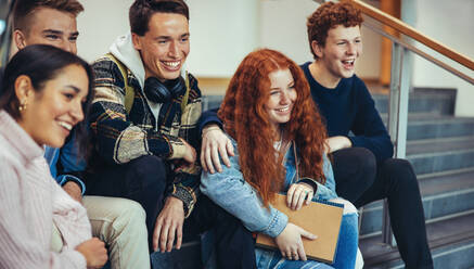 Studenten auf einer Treppe, die wegschauen und lächeln. Junge Männer und Frauen sitzen auf einer Treppe in einem College-Campus. - JLPSF07066