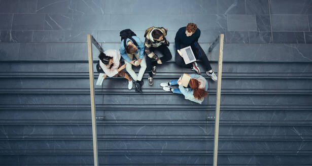 Young people at college during break time. Boys and girls sitting on stairs in university campus. - JLPSF07071