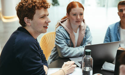 Männlicher Student im Gespräch mit Freunden in der Universität, während er gemeinsam studiert. Junge Leute in einer Studiengruppe an der Universität. - JLPSF07086