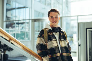 Student auf College-Treppe lächelnd. Junger Mann lächelt in die Kamera, während er am Treppengeländer in der Universität lehnt. - JLPSF07090