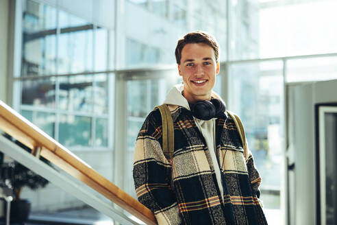 Student at college stairs smiling. Young man smiling at camera while leaning at stairs railing in university. - JLPSF07090