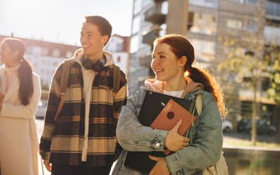 Friends looking away while walking outdoors with friends in college. Cheerful students walking in university outdoors. - JLPSF07097