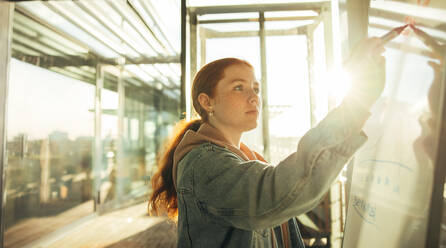 Student writing on whiteboard. Young woman studying in college. - JLPSF07104