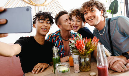 Eine liebevolle Gruppe von Freunden macht ein Selfie, während sie beim Mittagessen zusammensitzen. Eine Gruppe junger queerer Menschen, die in einem Restaurant fröhlich lächeln. Freunde, die zusammenkommen und Zeit miteinander verbringen. - JLPSF07135