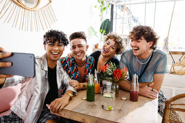 Vier Freunde machen ein Selfie, während sie beim Mittagessen zusammensitzen. Eine Gruppe junger queerer Menschen lächelt fröhlich in einem Restaurant. Freunde, die sich zusammenschließen und Zeit miteinander verbringen. - JLPSF07137
