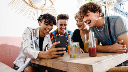 Vier junge Leute, die während des Mittagessens ihre Freunde per Video anrufen. Eine Gruppe fröhlicher Queer-Freunde, die in einem Restaurant zusammensitzen. Freunde, die zusammenkommen und Zeit miteinander verbringen. - JLPSF07138