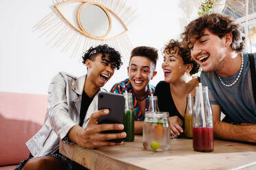 Lächelnde Gruppe von Freunden, die live online streamen, während sie in einem Restaurant sitzen. Eine Gruppe von vier jungen queeren Menschen, die während des Mittagessens Spaß miteinander haben. Freunde, die zusammenkommen und Zeit miteinander verbringen. - JLPSF07139