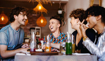 Unbeschwerte Gruppe von Freunden, die in einem Restaurant zusammen lachen. Vier junge Queer-Leute, die sich beim Mittagessen amüsieren. Freunde, die zusammenkommen und Zeit miteinander verbringen. - JLPSF07142