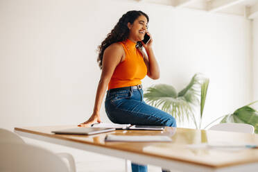 Erfolgreiche Geschäftsfrau lächelt glücklich, während sie mit ihren Geschäftspartnern telefoniert. Fröhliche junge Geschäftsfrau, die an einem modernen Arbeitsplatz Geschäftspläne macht. - JLPSF07195