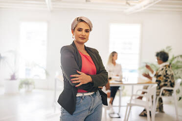 Young businesswoman looking at the camera while standing in a modern meeting room. Confident young businesswoman attending a meeting with her team in an all-female office. - JLPSF07229