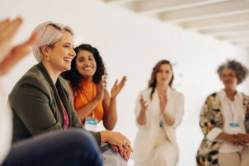 Lächelnde Geschäftsfrauen, die ihren Kolleginnen während einer Konferenz an einem modernen Arbeitsplatz applaudieren. Eine Gruppe erfolgreicher Geschäftsfrauen, die in einem Startup nur für Frauen arbeiten. - JLPSF07261