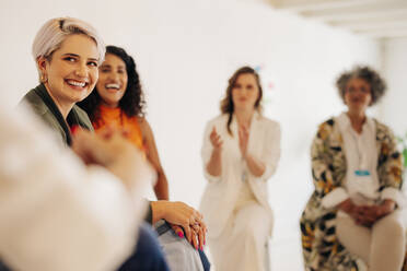 Geschäftsfrauen applaudieren ihren Kolleginnen während einer Konferenz an einem modernen Arbeitsplatz. Eine Gruppe erfolgreicher Geschäftsfrauen arbeitet in einem Start-up-Unternehmen zusammen, das ausschließlich von Frauen geführt wird. - JLPSF07262