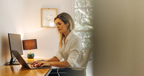Junge Geschäftsfrau, die in ihrem Heimbüro auf einem Laptop tippt. Unternehmerin, die von zu Hause aus eine E-Mail an ihre Geschäftskunden schreibt. - JLPSF07278