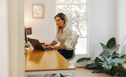 Unternehmerin tippt auf einer Laptop-Tastatur, während sie in ihrem Büro sitzt. Konzentrierte junge Geschäftsfrau schreibt eine E-Mail an ihre Geschäftskunden. - JLPSF07279